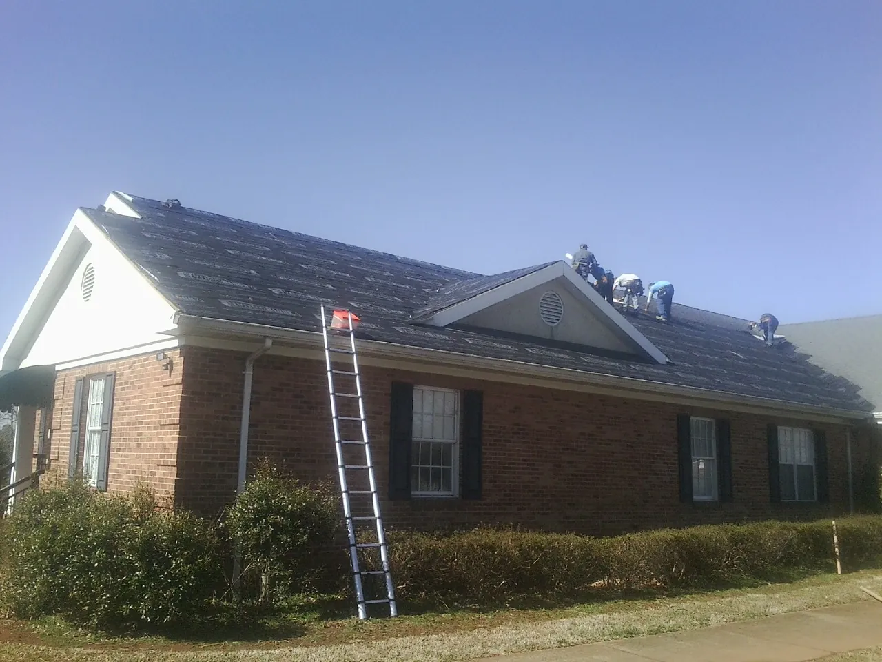 Crew tearing shingles off a brick ranch roof with a ladder set — Metal Roof Repair work by our crew in Glencoe