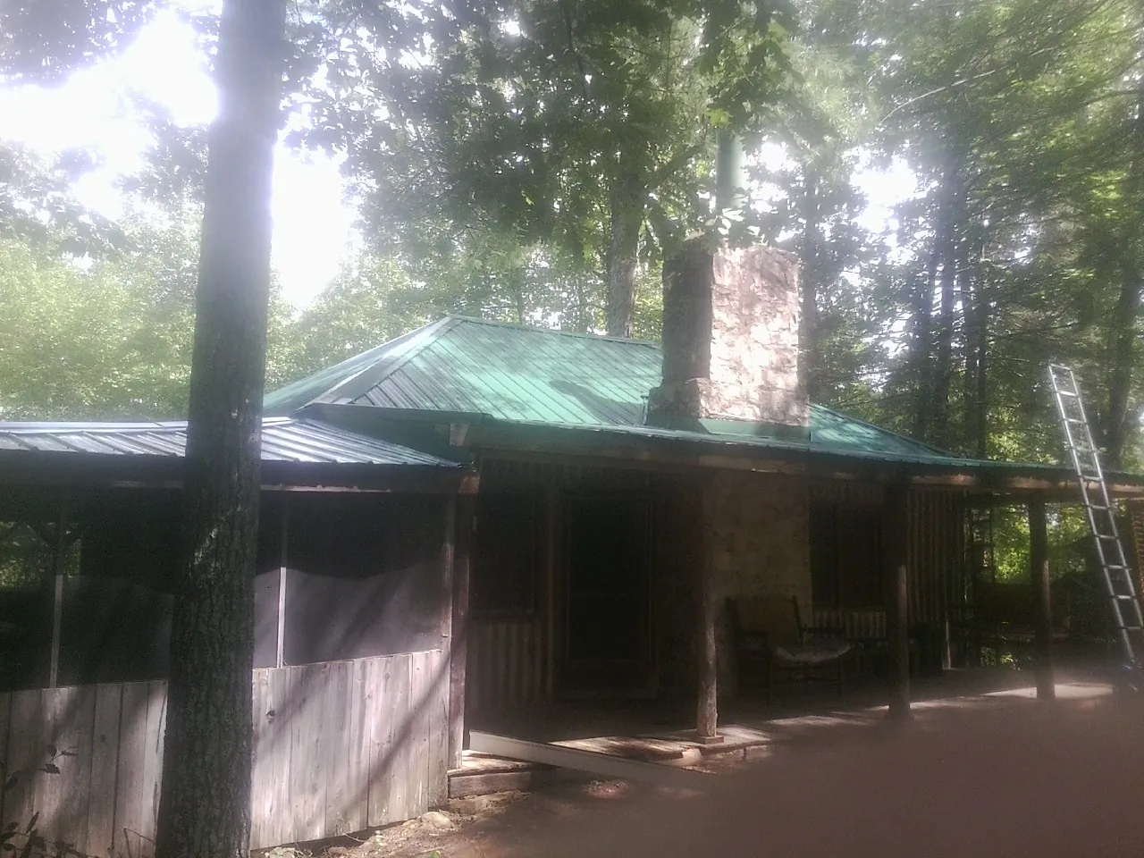 Green metal roof and stone chimney above a log cabin porch in Glencoe